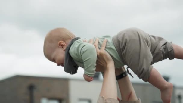 赤ん坊の息子を持ち上げて頬にキスする陽気な若い母親のゆっくりとした動きを傾けて — ストック動画