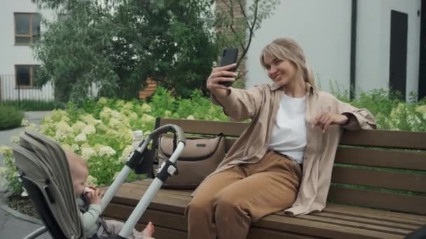 Junge Kaukasische Mutter Sitzt Auf Bank Und Macht Selfie Foto — Stockvideo