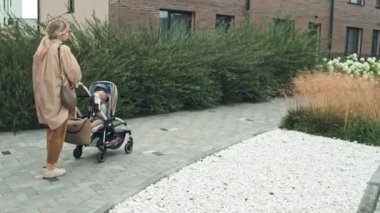 Rahat bir kıyafet giymiş genç bir kadının bebeğiyle bebek arabasında yürürken görüntüsü.