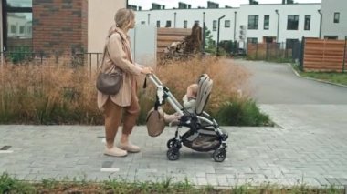 Yan görüntüde, genç anne şık bir kıyafet giyerken sokak boyunca küçük oğluyla bebek arabasında yürürken görülüyor.