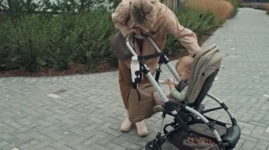 Modern beyaz anne, bebek arabasının kaputunu tamir etmek için bebeğiyle dışarıda vakit geçiriyor.