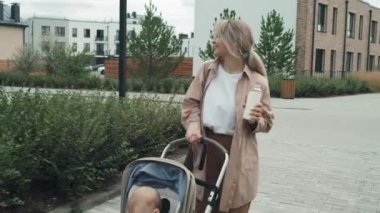 Modern genç anne bebeğini bebek arabasına iterken su içiyor.