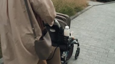 Sarı saçlı, sıradan kıyafetler giyen, bebekle bebek arabasında yürüyen genç bir kadın.