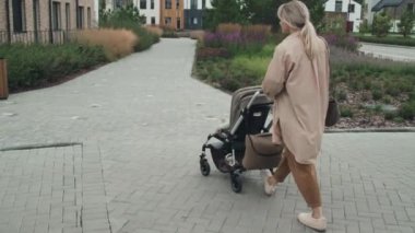 Modern genç annenin bebeğiyle dışarıda yürürken çekilmiş uzun bir görüntüsü.