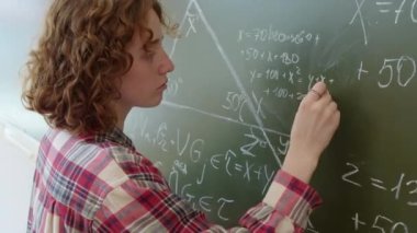 Çalışkan, kızıl saçlı, günlük kıyafetler giyen, üniversitede okuyan, tahtada matematik problemi çözen beyaz kız.