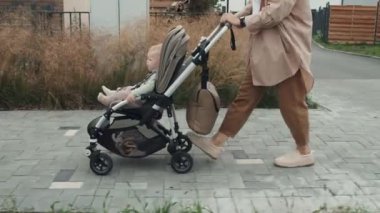 Yan görüş, genç annenin günlük giysiler içinde bebeğiyle sokakta yürüdüğünü gösteriyor.
