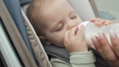 Bebek arabasında oturup açık hava şişesinden mama içen güzel bebeğin yakın plan portresi.