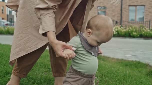 風の強い夏の日に芝生を歩いている間 赤ちゃんの息子を支える現代の若い母親のミディアムショット — ストック動画