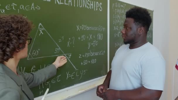 Matematik Öğretmeninin Siyah Erkek Öğrencinin Tahtaya Yazılan Problemi Çözmesine Yardım — Stok video