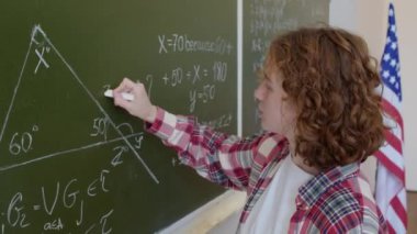 Üniversitedeki derste tahtada geometri problemi çözen kendine güvenen kızıl saçlı bir kızın orta boy yakın çekimi.