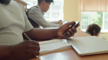Sınıfta notlar alırken akıllı telefon kullanan Afro-Amerikan üniversite öğrencisinin seçici odak noktası.