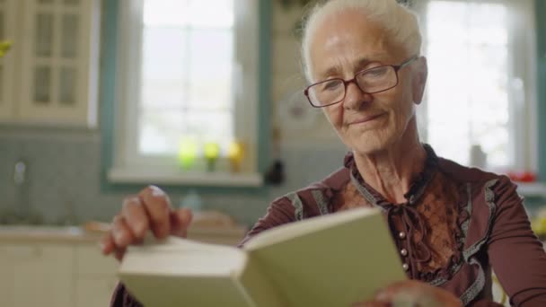 ホームリーディングブックで時間を過ごすシニア女性の選択的なフォーカス中クローズアップショット おばあちゃんコアコンセプト — ストック動画