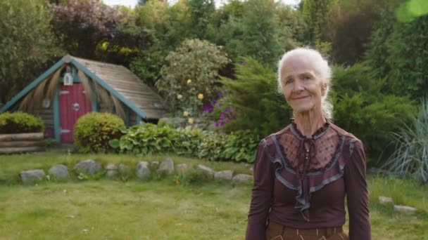 カメラを見ている美しいカントリーハウス裏庭に立っている美しい祖母の肖像画 ゴブリンコア美学 — ストック動画