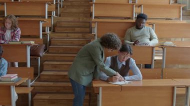Üniversite öğretmeni çok ırklı öğrencilerini kontrol ediyor, ödevlerini tamamlıyor ve ders sırasında hataları düzeltmelerine yardım ediyor.