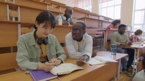 Afroamerikaner Sitzt Hörsaal Schreibtisch Und Hilft Seinem Asiatischen Klassenkameraden Bei — Stockvideo