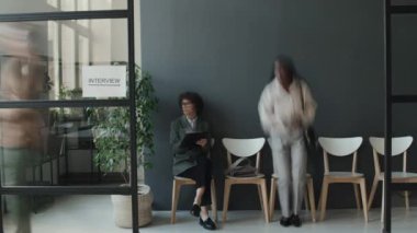 Siyahi ve Kafkasyalı kadın ve erkeklerin sırada oturup, ellerinde CV 'lerle yazışmaları, gelişleri, gidişleri, röportaj beklemeleri.