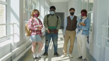 Modern etnik çeşitlilikte üniversite öğrencileri koridorda kameraya bakarken koruyucu maskeler takıyor.