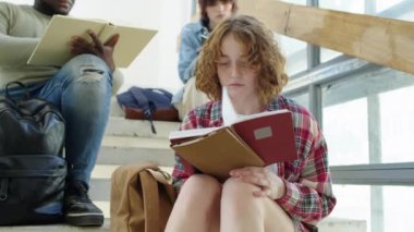 Merdivenlerde oturmuş ders notlarını okuyan çalışkan üniversite öğrencilerinin düşük açılı seçici odak noktası.