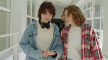 Kolej koridorunda yürürken sohbet ederken orta uzunluktaki iki beyaz kızın görüntüsü.