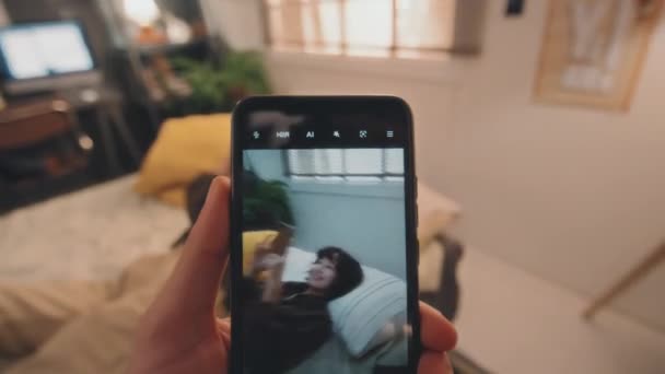 彼女がベッドに横たわっている間 スマートフォンで若い女の子を撮影する若い男の選択的な焦点Povショット スマートフォンで自分自身を撮影 彼女の顔をカバーしようと — ストック動画