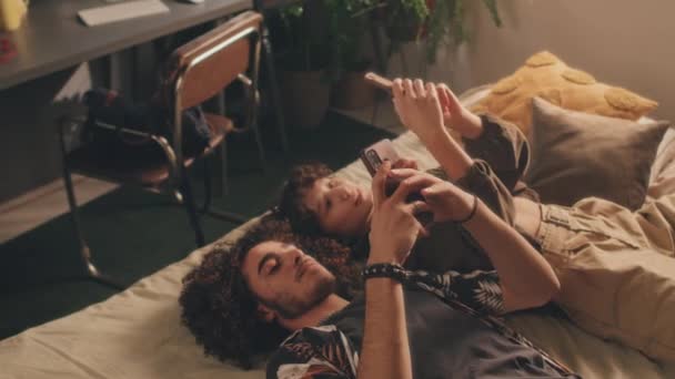 Genç Çiftin Telefonlarıyla Yatakta Yatıp Ekranlarını Birbirlerine Gösterip Gülümsedikleri Yüksek — Stok video