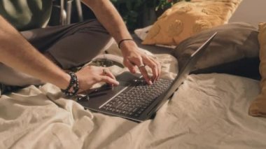 Erkek eli kelepçeli, yüzüklü, dizüstü bilgisayarda, yastıklarda, arka planda, sabahleyin dizüstü bilgisayarda yazan...