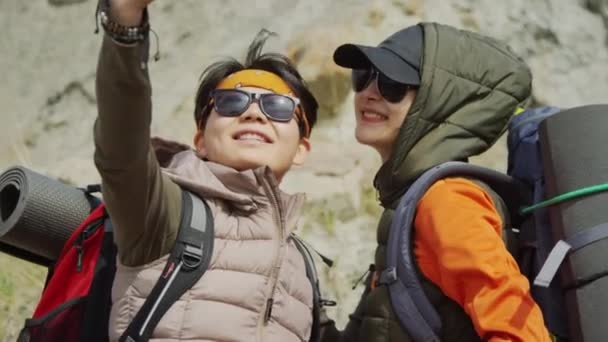サングラスで2人のアジア人女性観光客が スマートフォンカメラでセルフィーを作り 微笑んでいる バックグラウンド 昼間のロック — ストック動画