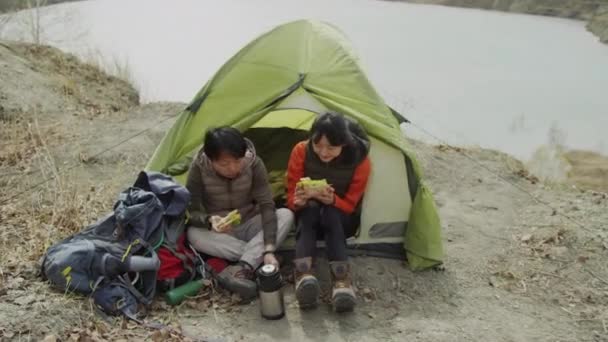 Pełne Ujęcie Dwóch Azjatyckich Przyjaciółek Siedzących Przy Wejściu Namiotu Jedzących — Wideo stockowe