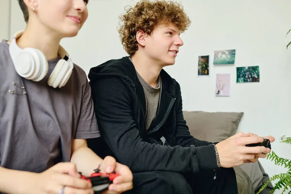 彼のガールフレンドの隣に座ってコンピュータ画面を見ている間 ジョイスティックのボタンを押すカジュアルウェアのティーンエイジャーの笑顔に焦点を当てます — ストック写真