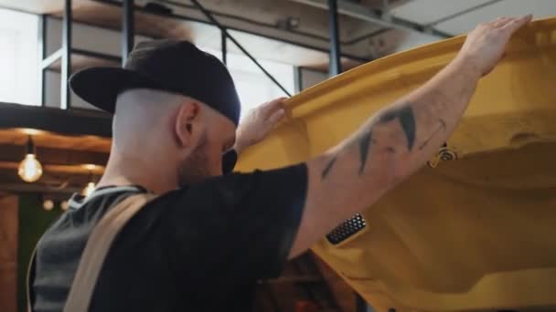 Наклонись Поближе Татуированному Автомеханику Закрывающему Капот Желтой Машины После Осмотра — стоковое видео