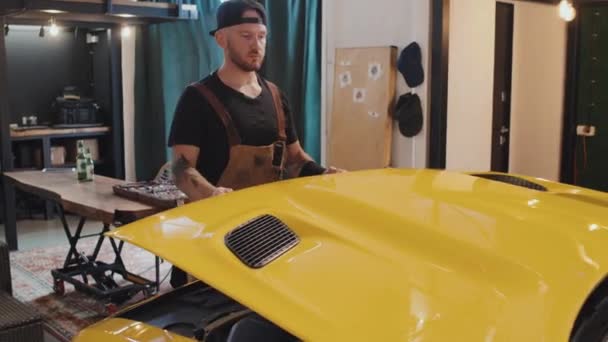 Tiro Médio Mecânico Tatuado Vestindo Macacões Abrindo Capuz Motor Amarelo — Vídeo de Stock