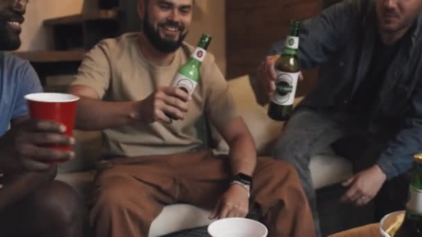 リビングルームのソファーに座っているボトルとカップに触れる3人の男性の友人の中型のフロントショット — ストック動画