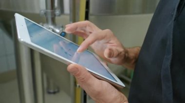 Kırmızı saçlı ve sakallı, bira mayalama tankının yanında duran, dokunmatik ekran tableti üzerinde çalışan ve kontrol göstergelerine bakan beyaz erkek bira ustasının yakın çekimde çekilmiş resimleri.