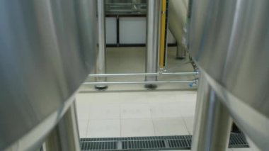 Önlüklü, bira fıçısı dolusu taze bira taşıyan, büyük çelik fermenter tanklarının arkasından çekilen anonim bira fabrikası işçisinin bacakları ve alt gövdesinin kilitlenme sahnesi.