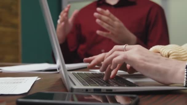 在会议室举行的商务会议上 在手提电脑键盘上快速打字的脸色苍白 难以辨认的女人和在后台说话的匿名同事的手像特写 — 图库视频影像