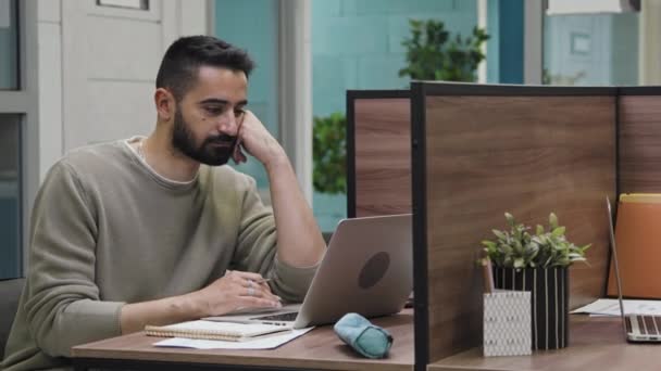 疲れた中東の男性フリーランサーの中型ショット コワーキングオフィスのノートパソコンで一人で座って インターネット上のデータを閲覧し 情報をスクロール — ストック動画