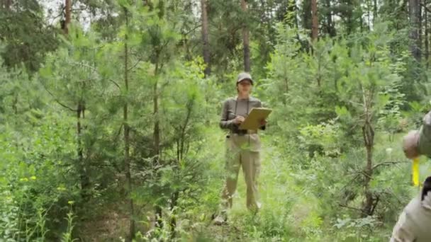 两名身穿卡其布制服的男女护林员检查自然保护区和谈话场所的松林 妇女在剪贴板上书写图表 男人拿着测量磁带 全景照 — 图库视频影像