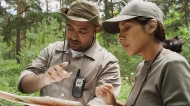 Yaz aylarında karışık yeşil ormanda duran melez erkek ve İspanyol çevre koruma memurlarının haritaya bakıp arazi araştırması planladıkları orta boy yakın plan çekimleri.