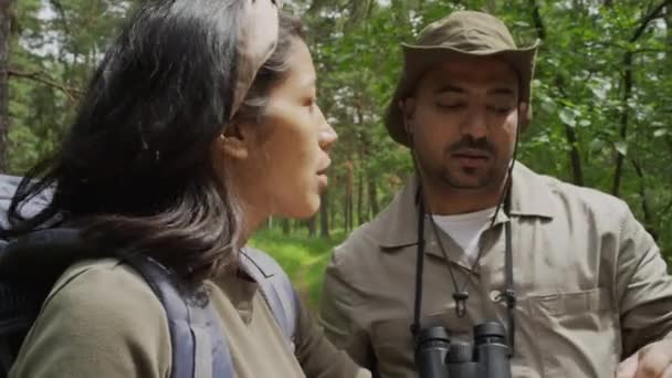 自然公園に立っているバックパックと若いヒスパニック系女性エコツーリズムのミディアムクローズアップショット 地図上の方向と指差している女性の森林レンジャーに耳を傾けます — ストック動画