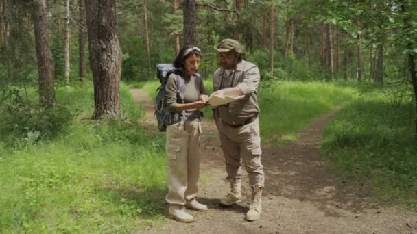 身着卡其布服装和公用事业裤的不同族裔男女在森林中交谈 女游客询问方向 地图上还显示了鸟类的男性森林 并指出了道路 — 图库视频影像