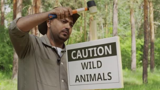 カーキの制服の中年インドの森林レンジャーのメディアロックダウンショットと 野生動物について警告する慎重なプラークでハンマーでハンマーで打つ太陽光浴 — ストック動画