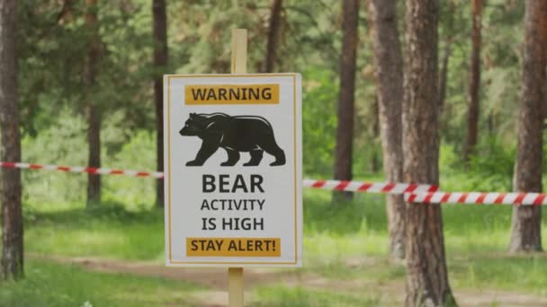 晴れた夏の日には森に囲まれた野生の熊の注意のプラークのクローズアップセレクティブなフォーカスショット 赤いバリケードテープはぼやけた背景で木の間に伸びました — ストック動画