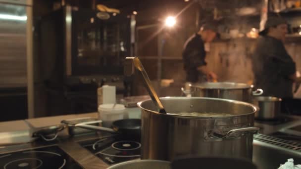 餐厅厨房感应炉上热蒸汤烹调钢锅中的特写镜头和背景不明的厨师 — 图库视频影像