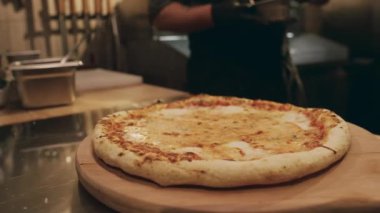 Lokanta mutfağında, ahşap tabakta duran taze peynirli pizzanın ve tanınmayan erkek şefin ellerinin kabuğa fırçayla yağ ya da tereyağı sürmesi.