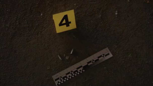 犯罪捜査中の殺人現場で地面に横たわる黄色い法医学マーカーのクローズアップハンドヘルドトップショット — ストック動画