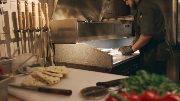 身着黑色制服 头戴手套 头戴围裙的白人男性厨师 站在餐厅厨房里 为传统的意大利披萨做着面团的造型和搅拌 — 图库视频影像