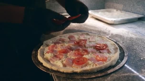 レストランのキッチンでピザを作っている間 ハムとグリードチーズの上にスライスされたトマトを置くブラックエプロンと手袋の匿名シェフのクローズアップショット — ストック動画