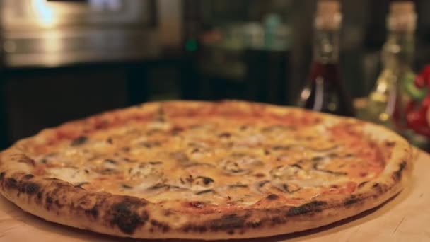 在餐厅厨房柜台上的木制盘子上旋转的新鲜烤 烤蘑菇和奶酪披萨 以及背景模糊的烤箱的特写选择性镜头 — 图库视频影像