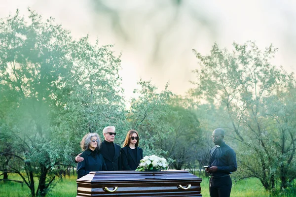 Long Shot Mourning Family Three Priest Black Attire Surrounding Wooden — Stock Photo, Image