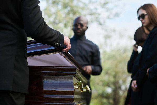 Close-up of man in black suit closing lid of coffin at funeral ceremony after farewell and saying last goodbye to dead person before burying